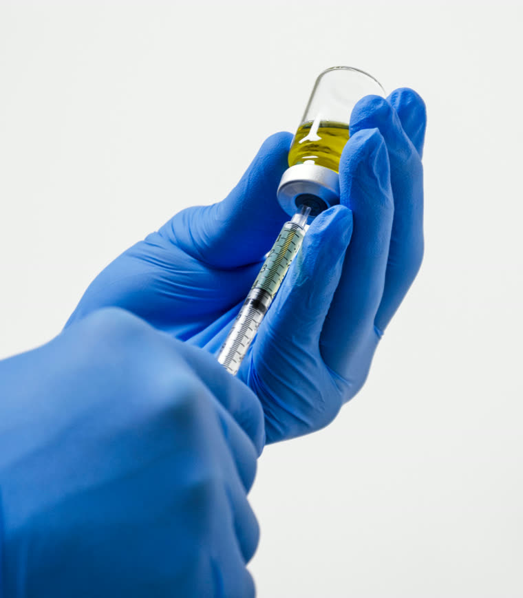Gloved hands drawing product from a vial into a syringe